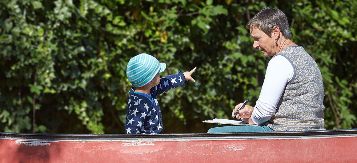 Eine Frau notiert etwas, während ihr ein Kind etwas in der Entfernung zeigt.